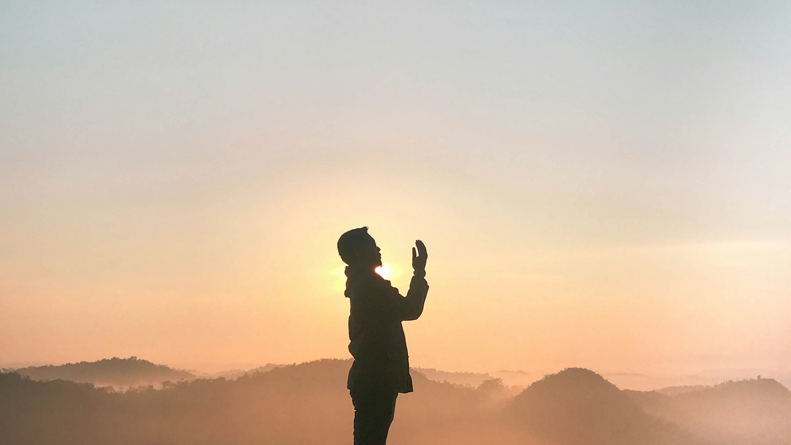 A person in quiet prayer against a sunset sky